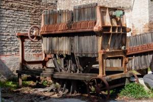 Τροχήλατο φιλτρό. Σκοπό είχε να απομακρύνει από τα κρασιά, την μπύρα, ή τα διάφορα άλλα οινοπνευματώδη τα αιωρούμενα στερεά σωματίδια. Τα φίλτρα ήσαν υφασμάτινα και συγκρατούντο σε ξύλινα τελάρα.Πολλά τέτοια τελάρα κρεμόντουσαν το ένα πισω από το άλλο σε αυτές τις οριζόντιες ραβδους και με τις βίδες εσφίγκοντο τόσο δυνατά ώστε να μην υπάρχει διαρροή υγρού μεταξύ τους. Η είσοδος του υγρού γινόταν από τον σωλήνα που φαίνεται στο επάνω μέρος και η έξοδος του από την κάτω σωλήνα πλέον καθαρό.  πηγή: Π. Τουλιάτος